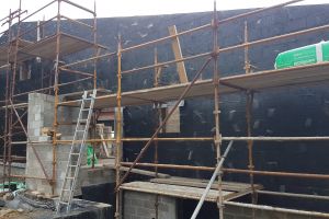 The north wall has been prepared for stone cladding with a waterproof coating of black bituminous paint. The upper floor porch is still under construction.