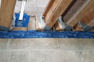 The wall behind the joist hangers (seen from below) has been parged, and now airtightness tape is applied along the top and bottom of the parged area, to ensure there are no breaks in the airtightness barrier.