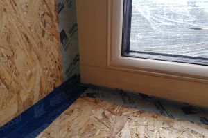 A close-up showing the airtightness tape lapping across from the OSB onto the edge of the window. Tape is also applied where the two pieces of OSB meet.